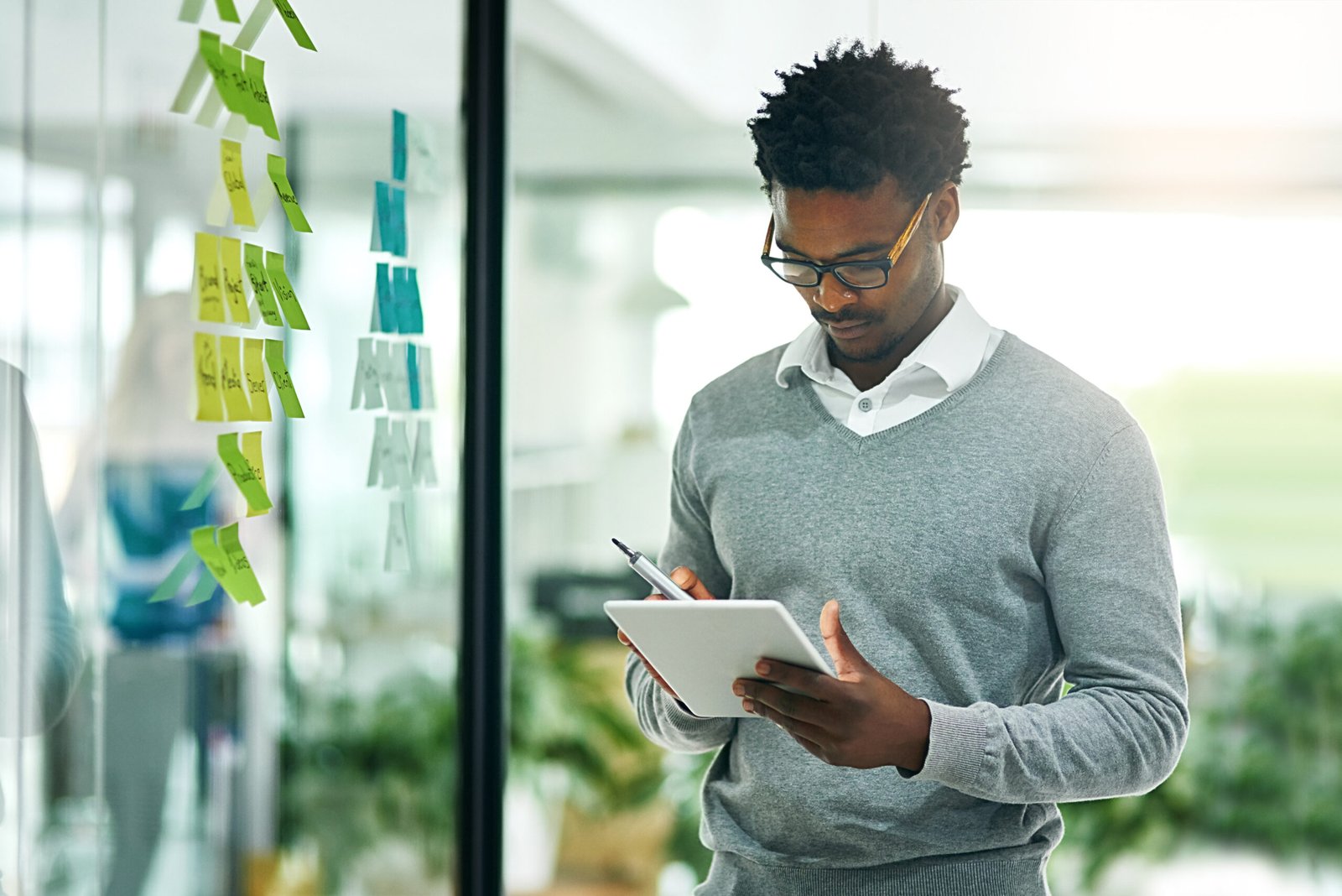 Glass wall, business tablet and black man planning, research and strategy in office workplace. Technology, board and African male professional with sticky notes for online, schedule and brainstorming.